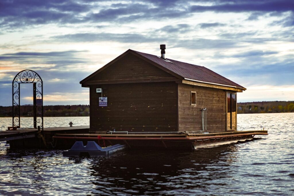 Floating wooden house on a serene river under a vibrant sunset sky.