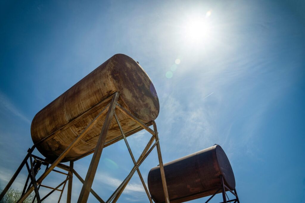 Rusty industrial oil tanks with a clear blue sky and bright sun.
