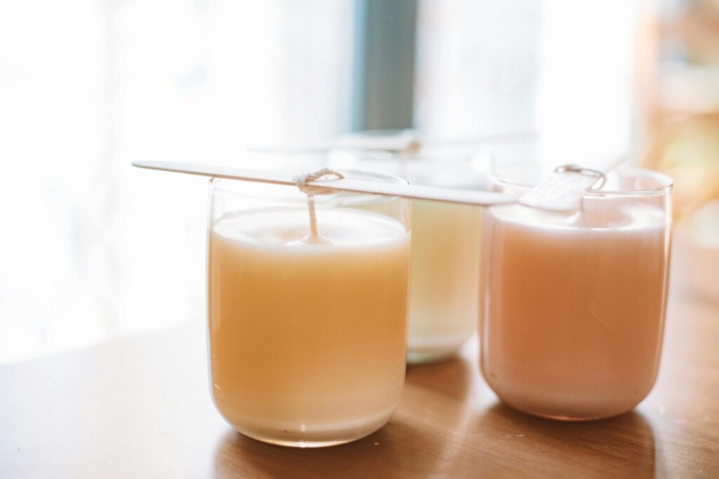 A still life of handmade candles in glass jars with wicks, captured in warm natural light.