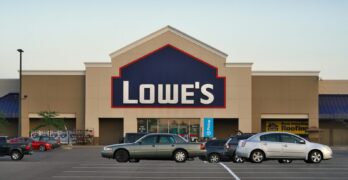Front view of a Lowe's store entrance with parked cars in the lot during the day.