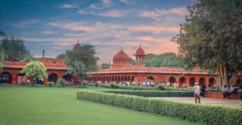 A scenic view of the Red Fort gardens in Delhi, showcasing its historic architecture and lush greenery at sunset.