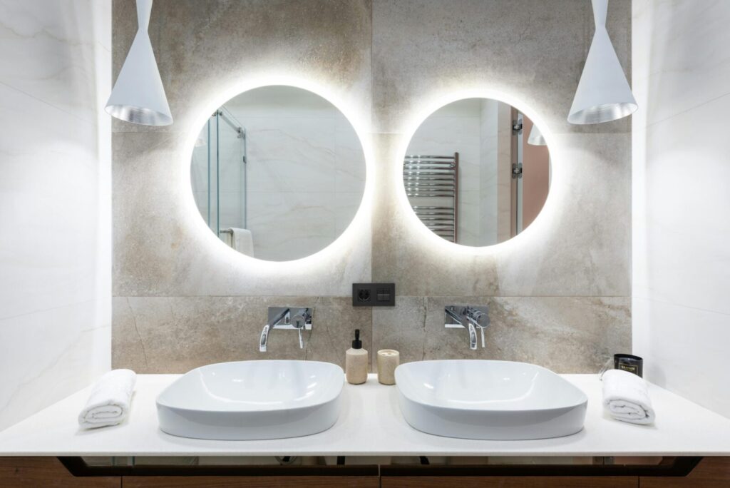 Contemporary bathroom design featuring a stylish double vanity with round backlit mirrors.
