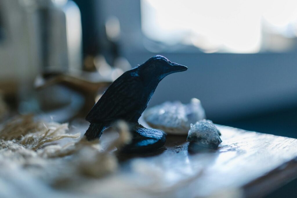 Close-up of a raven sculpture on a table with crystals and soft lighting, artistic theme.