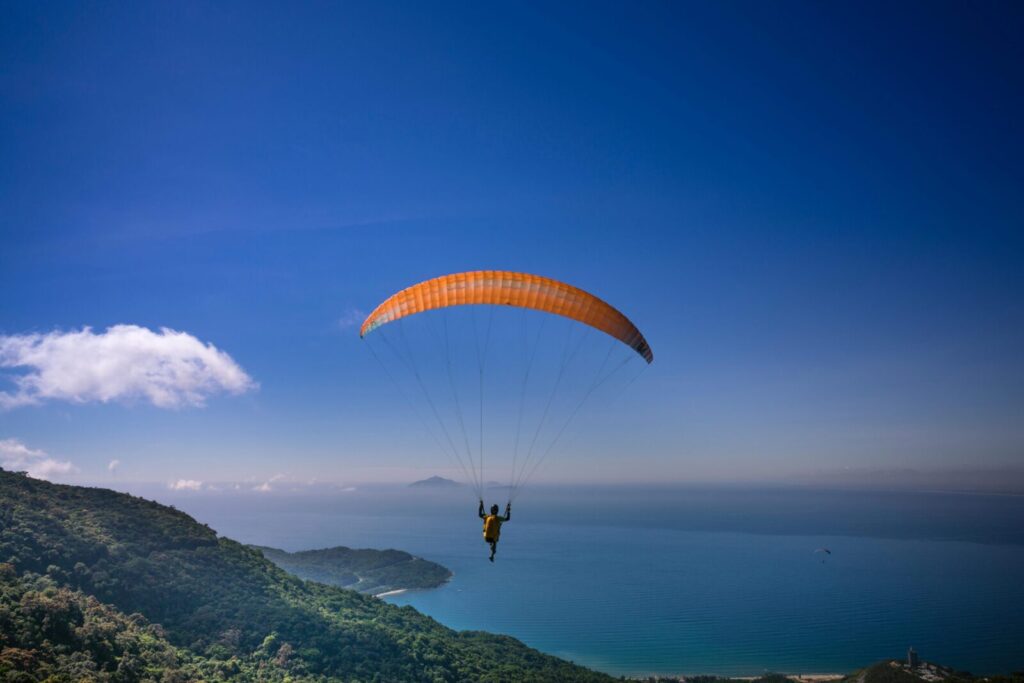 A lone paraglider flies over the ocean with a breathtaking view of the coastline and horizon.
