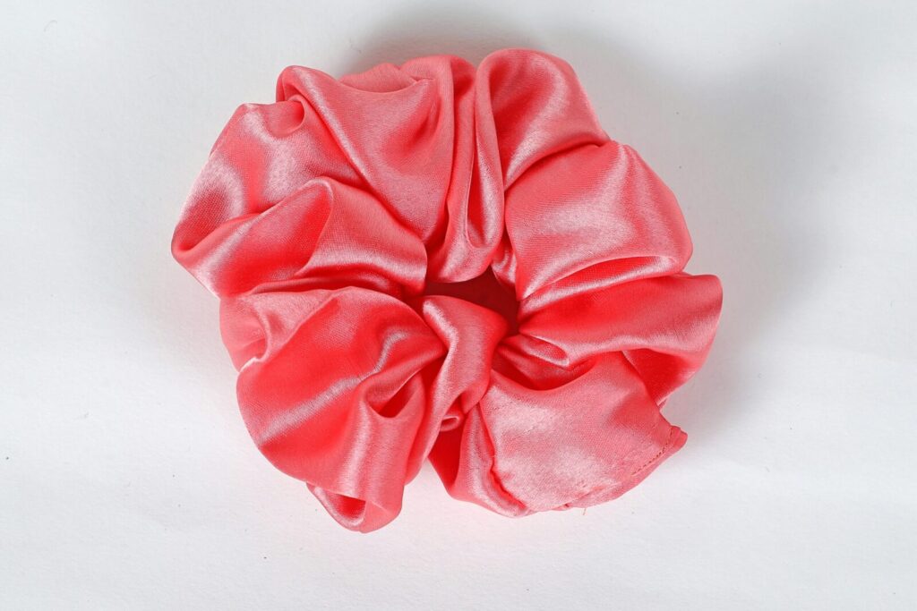 Vibrant pink satin scrunchie with detailed fabric folds close-up. Ideal for fashion and hair accessory related use.