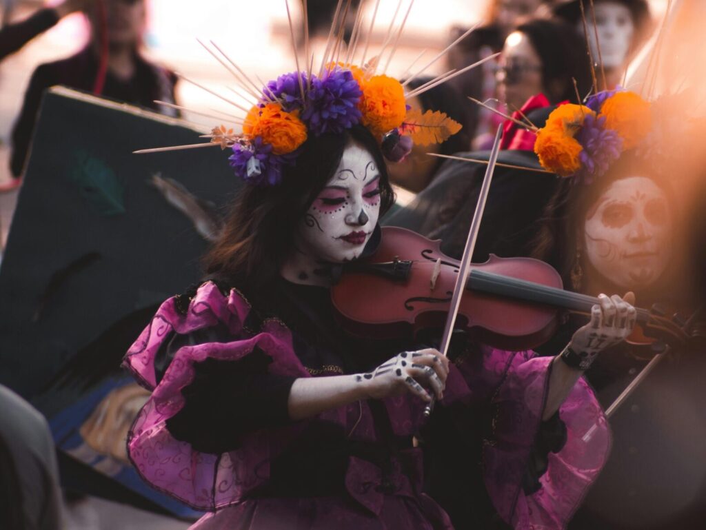 Colorful Day of the Dead celebration featuring a musician with skull makeup and vibrant floral headpiece.