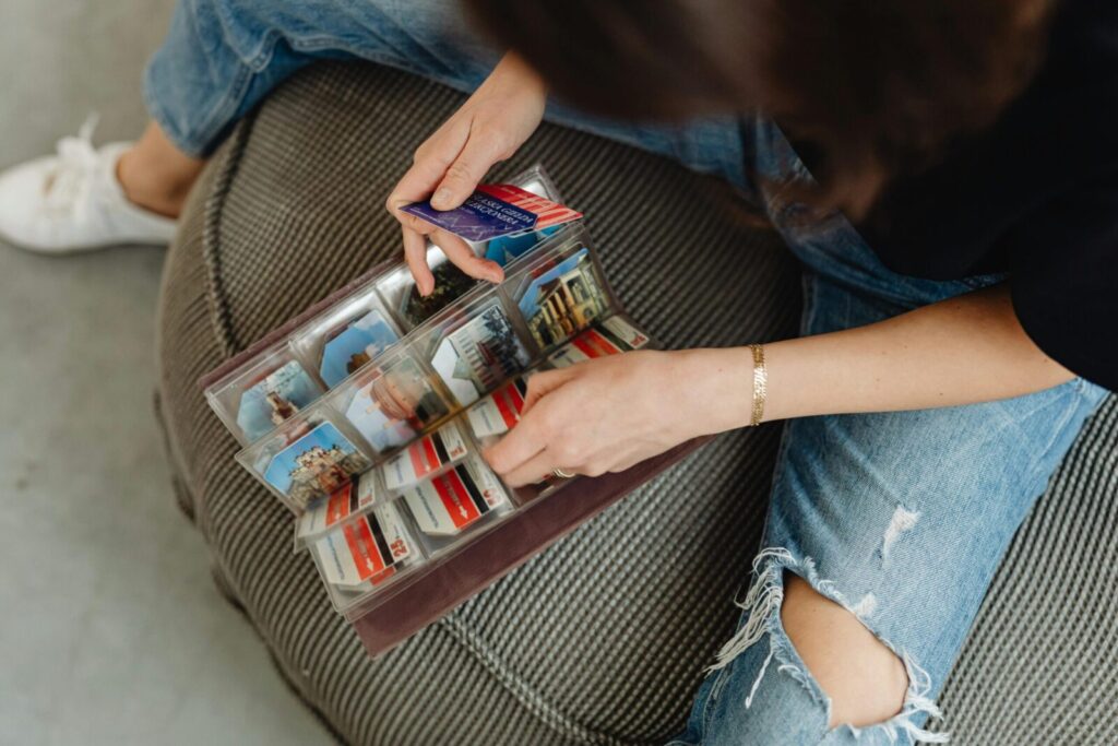 A person flipping through a photo album filled with travel souvenirs, sitting on a comfy chair.