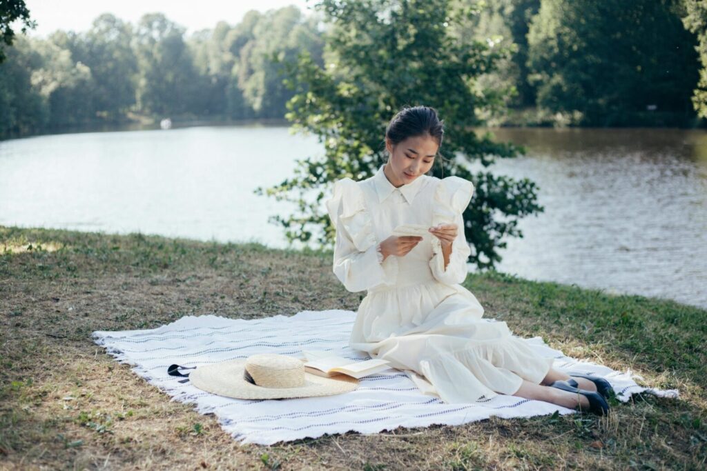 A woman in a white dress enjoys a peaceful afternoon reading by the river.