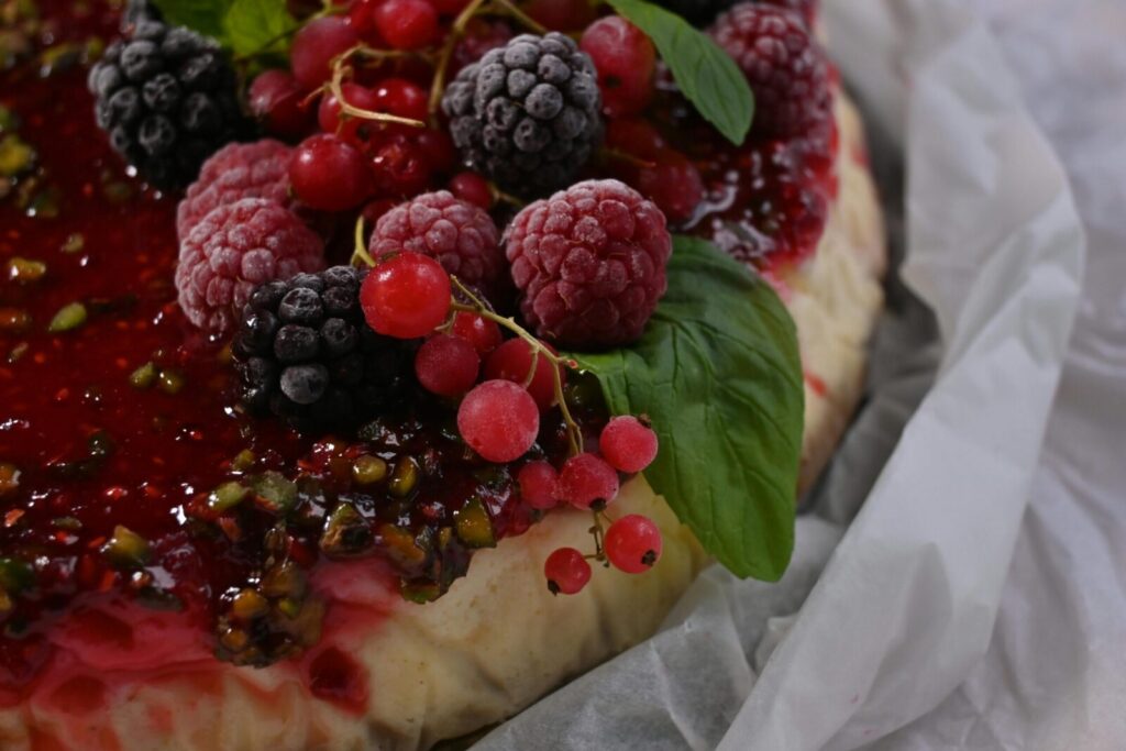Close-up of a tasty tart topped with fresh mixed wild berries and mint leaves.