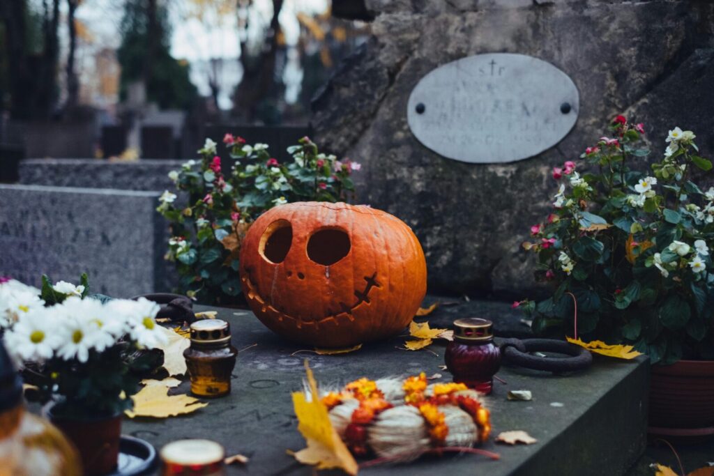 A spooky jack-o'-lantern on a grave surrounded by flowers and candles in a Warsaw cemetery.
