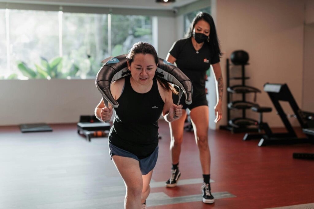 Two women focused on strength training in a Singapore gym with a personal trainer.