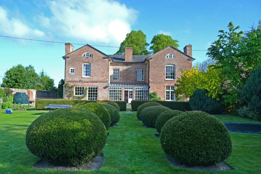 a large brick house with a lawn and hedges in front of it with Moseley Old Hall in the background