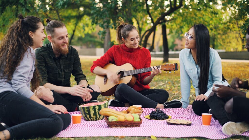Friends enjoying a picnic and playing guitar in park.