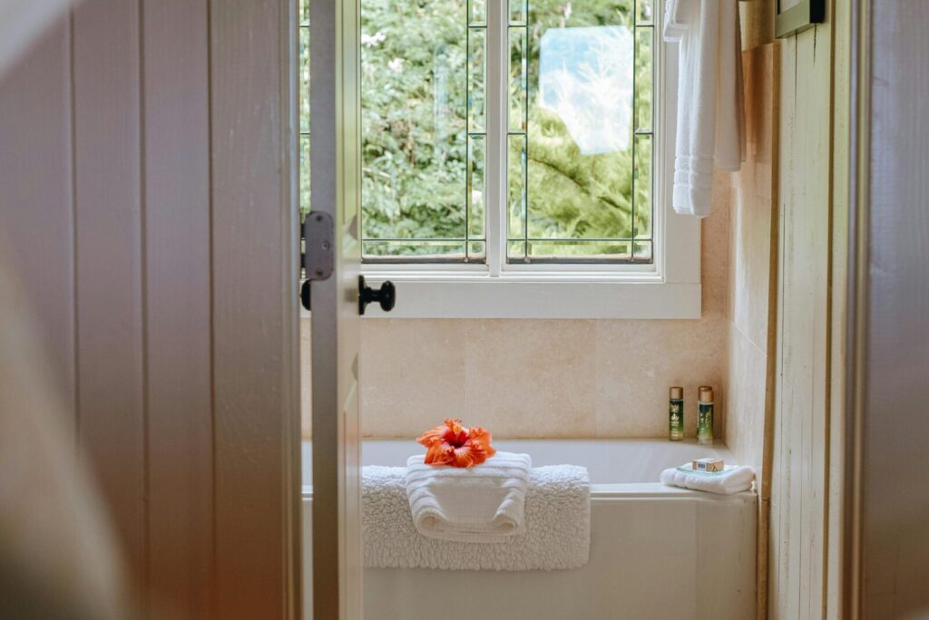 Clean light bathroom with window with view of green plants placed near bath in modern resort hotel