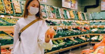 Woman wearing a face mask choosing fruits in a supermarket for safe shopping during pandemic.