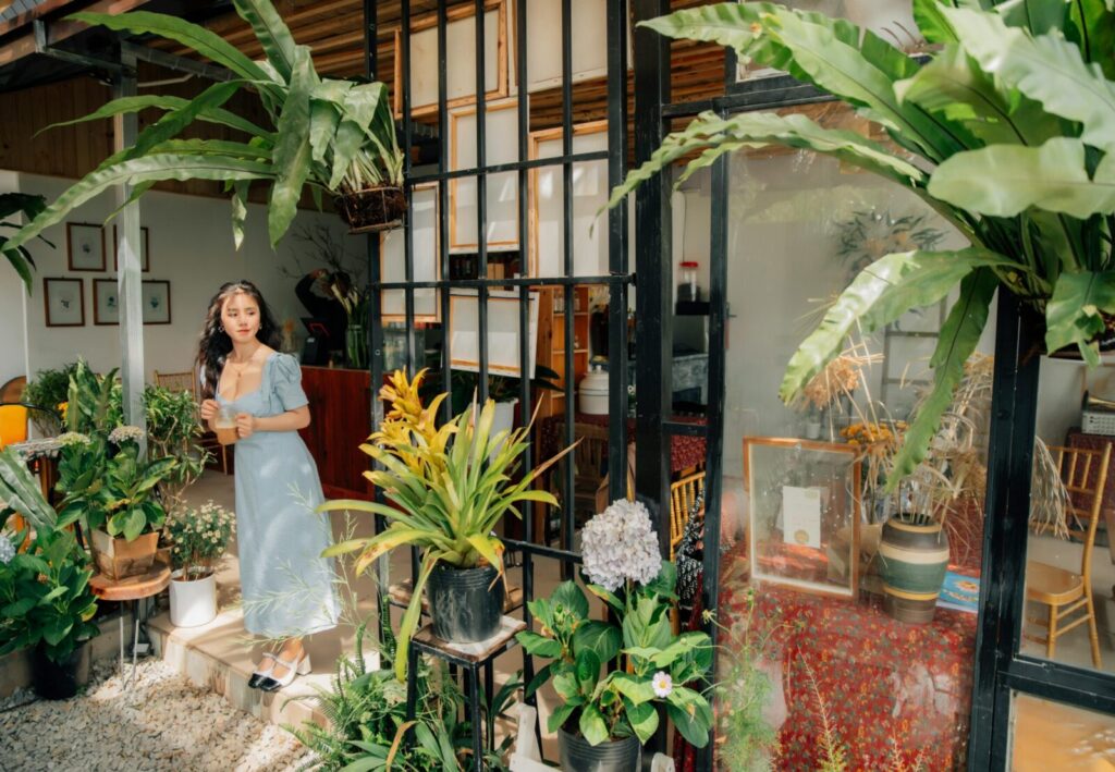 A woman in a blue dress standing amidst vibrant houseplants, enjoying the natural ambiance.