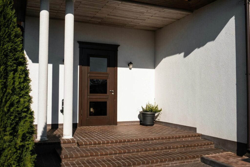 Contemporary house entrance featuring brown door, brick steps, and decorative columns.