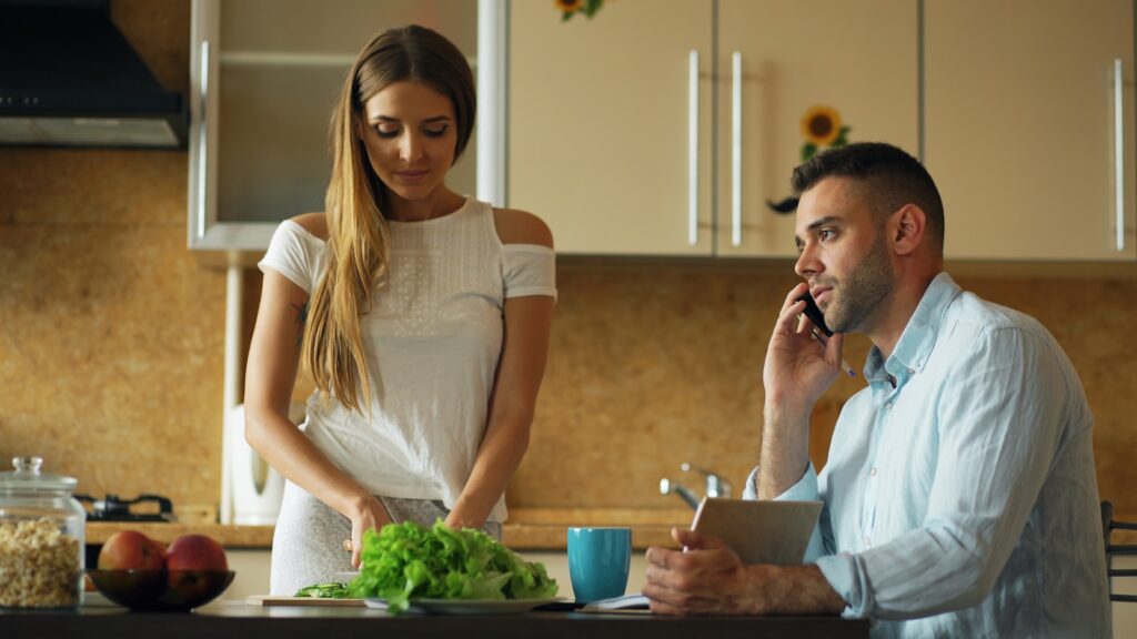 Couple in kitchen, woman chopping lettuce, man on phone.