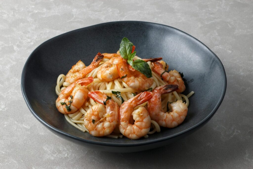 A tantalizing dish of shrimp pasta garnished with fresh herbs in a dark ceramic bowl.