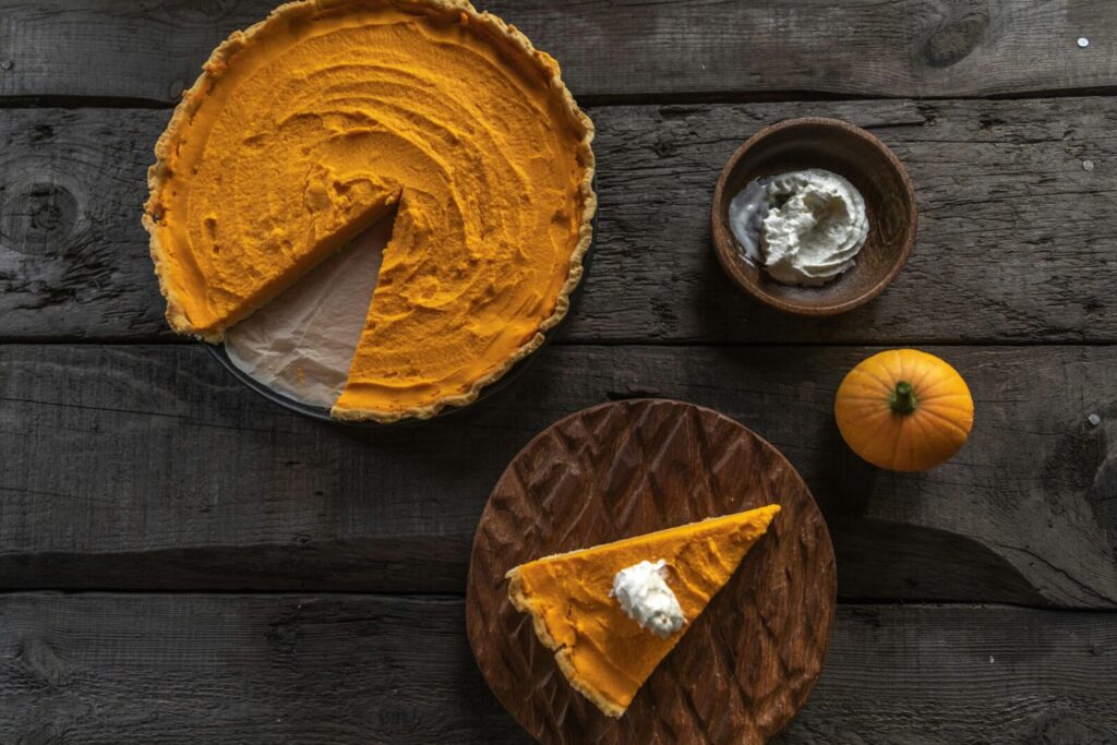 Top view of a pumpkin pie on rustic wood with whipped cream and a small pumpkin.