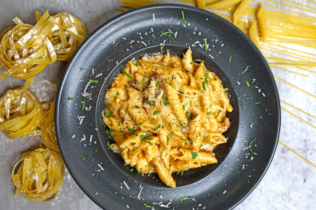 Top view of creamy pasta with cheese and herbs on a black dish.