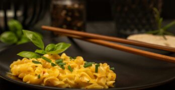 Delicious creamy pasta garnished with basil and chives, served on a black plate with chopsticks.