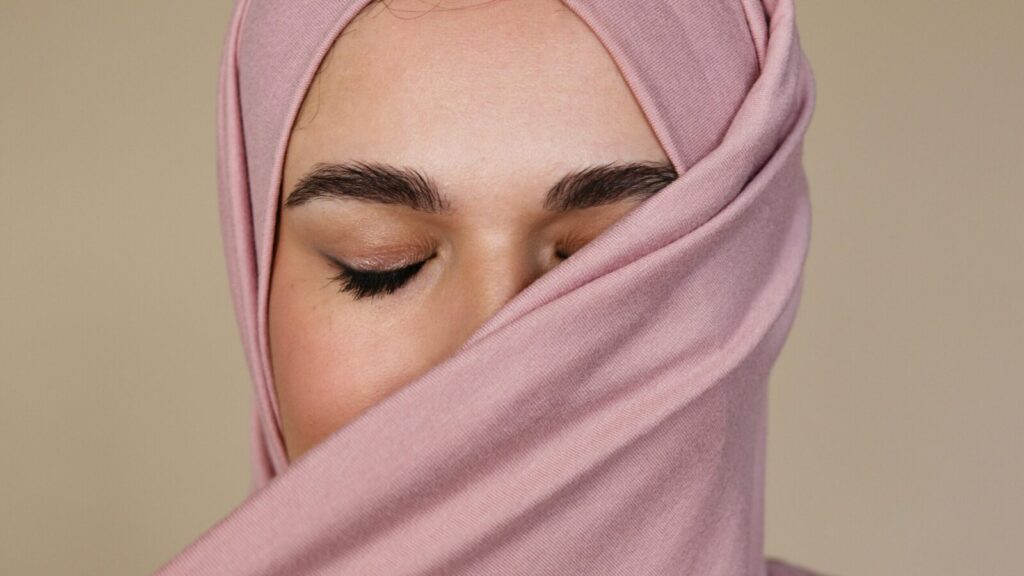 A serene close-up of a woman with closed eyes wearing a pink hijab, showcasing beauty and elegance.