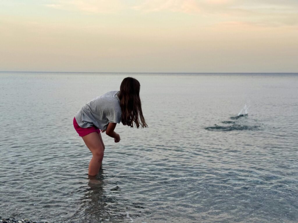 Young girl skipping stones on the tranquil Leptokarya beach during sunset, Greece.