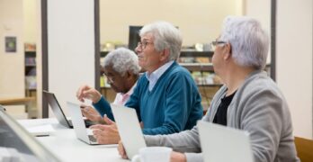 Elderly men using laptops in a modern tech class, learning digital skills.