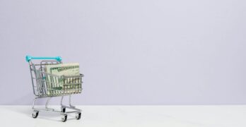Shopping cart filled with cash on a plain background, ideal for finance and retail themes.