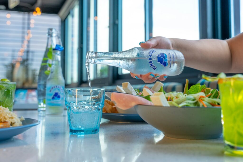 a person pouring water into a bowl of salad