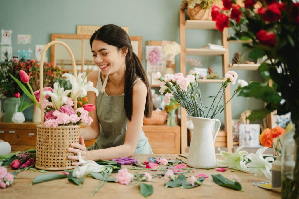 Smiling female florist arranging flower bouquet in a studio, surrounded by vibrant florals.