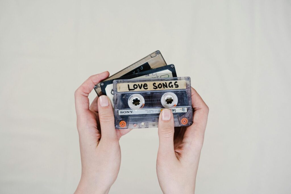 Hands holding cassette tapes labeled 'Love Songs', highlighting 90s nostalgia.