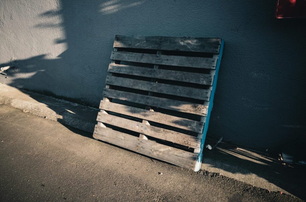 A wooden pallet leaning against a concrete wall casting shadows in daylight.