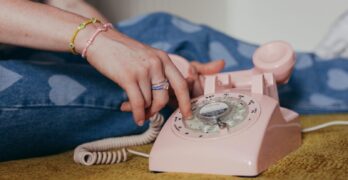 Close-up of a person dialing on a pink rotary phone, evoking a sense of nostalgia and retro charm.