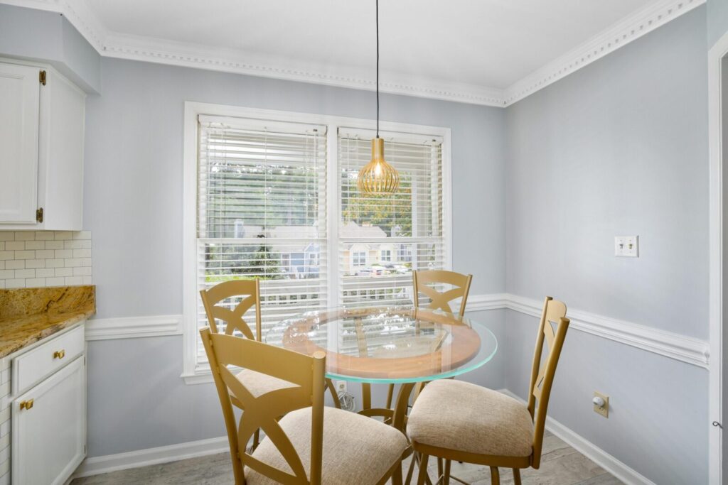 Bright and elegant dining room featuring a glass table and wooden chairs under a decorative ceiling lamp.
