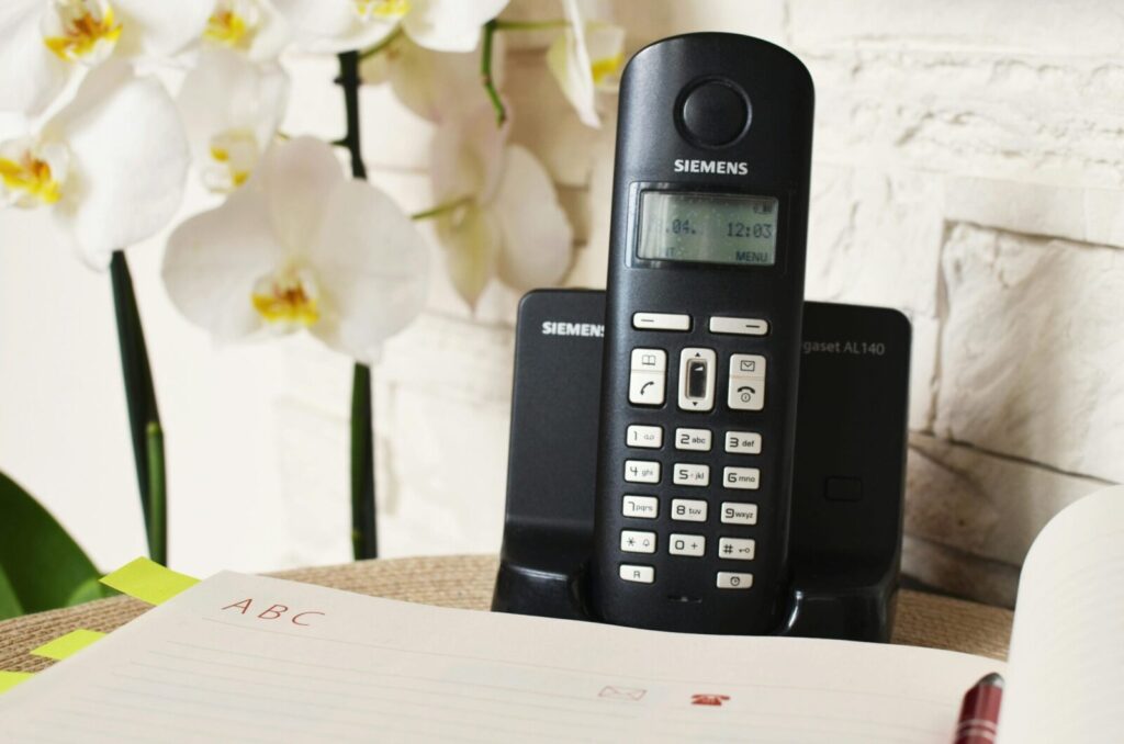 Close-up of Siemens cordless phone on a desk with a notebook and orchids in an indoor setting.