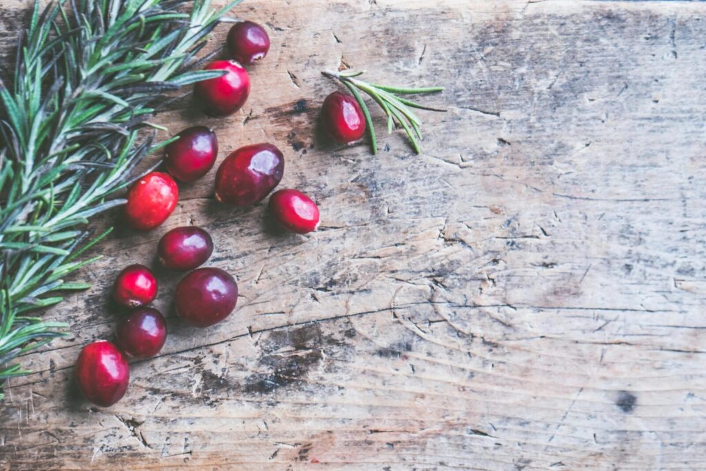 Top view of cranberries and rosemary on a rustic wooden surface, perfect for holiday themes.