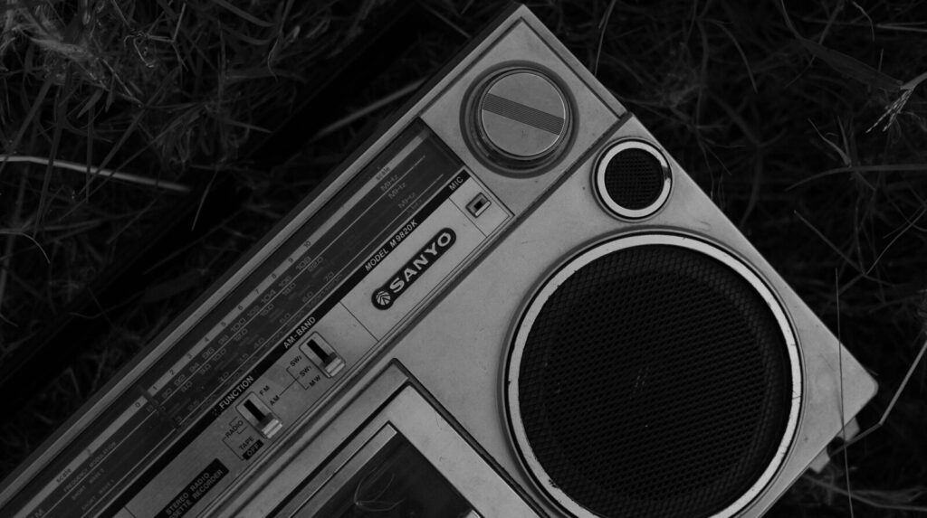Black and white photo of a vintage Sanyo boombox on grass, evoking nostalgia and old-fashioned charm.