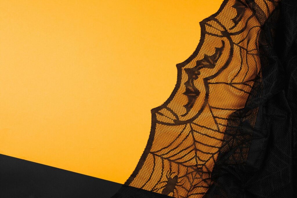 A detailed black lace pattern resembling cobwebs against a vibrant yellow backdrop, evoking Halloween themes.