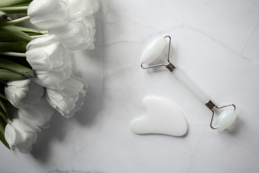 White tulips with jade roller and gua sha on marble for a calming skincare routine.