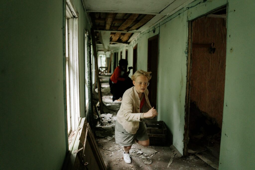 Two children in an abandoned building, exploring and showing curiosity amidst ruins.