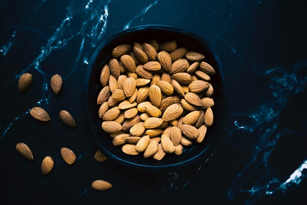 Aesthetic photo of healthy almonds in a black bowl on a marble surface.