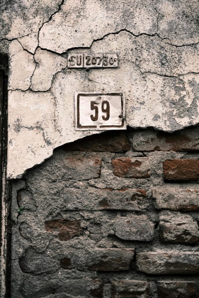Detail of an old brick wall with weathered plaster and a prominent number 59 sign.