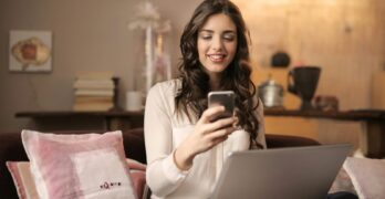 A woman enjoying leisure time using her smartphone and laptop in a cozy living room.
