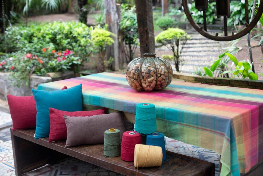Bright garden setting featuring a colorful table, threads, and cushions.