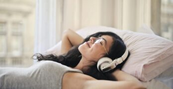 A woman with headphones lying on a bed, enjoying music in a relaxed, cozy setting.
