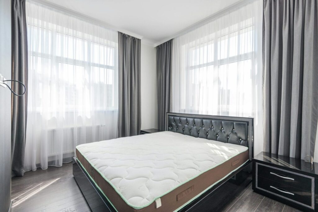 A bright and modern bedroom with a stylish bed, sheer curtains, and minimal decor.