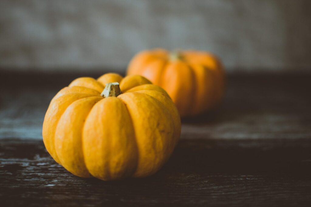 Two small orange pumpkins on a dark wooden surface, highlighting autumn vibes.