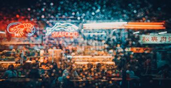 Explore the neon-lit ambiance of a bustling seafood market in Kuching at night, captured through a rain-splattered lens.